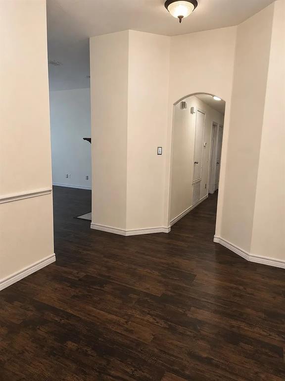 Interior space featuring dark wood-finish flooring, neutral wall tones, a prominent arched doorway, and a ceiling-mounted light fixture