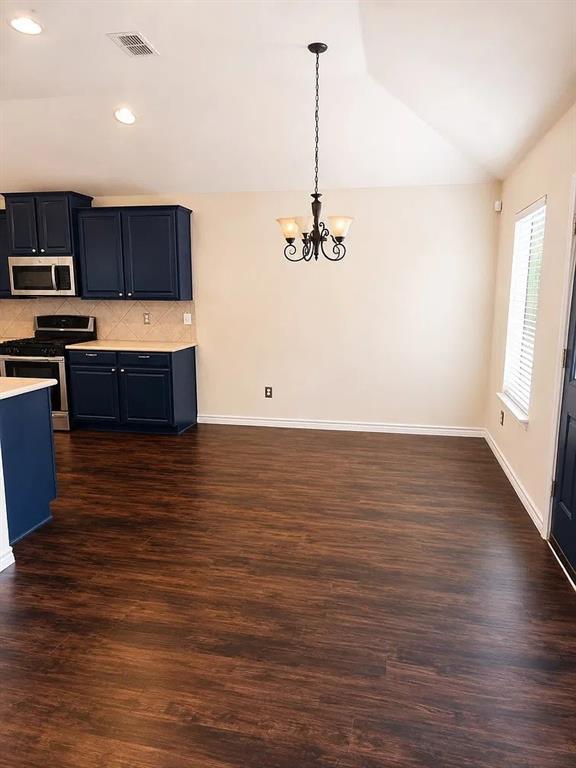 Kitchen featuring dark blue cabinetry, wood-finish flooring, vaulted ceilings, and a decorative wrought-iron chandelier Kitchen featuring dark blue cabinetry, wood-finish flooring, vaulted ceilings, and a decorative wrought-iron chandelier