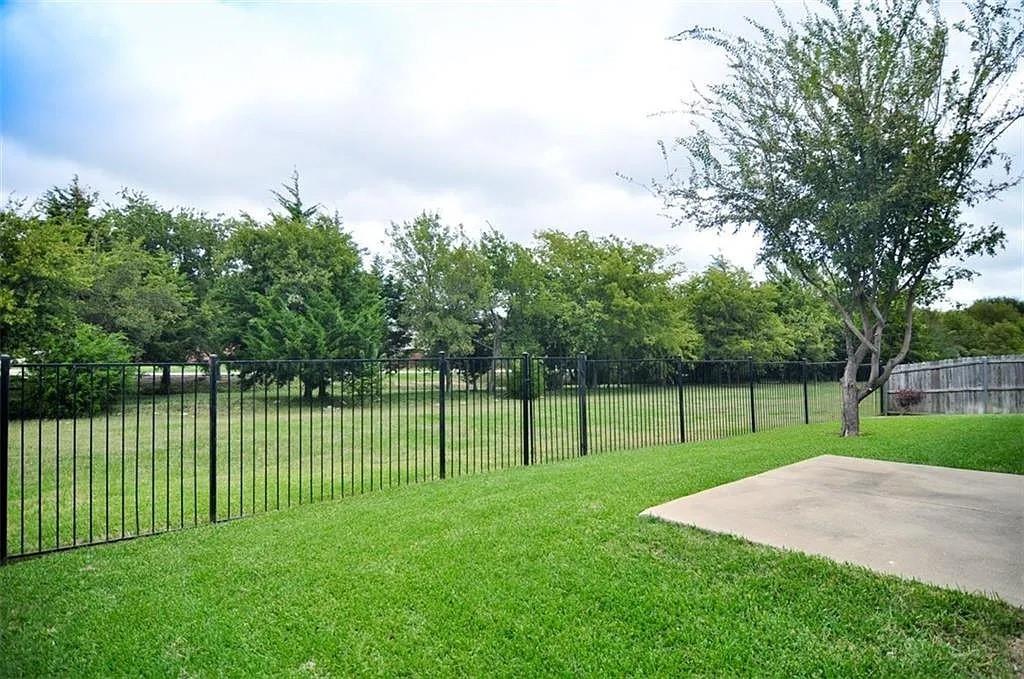 Expansive backyard featuring a level lawn, concrete patio, black metal fencing, and mature trees