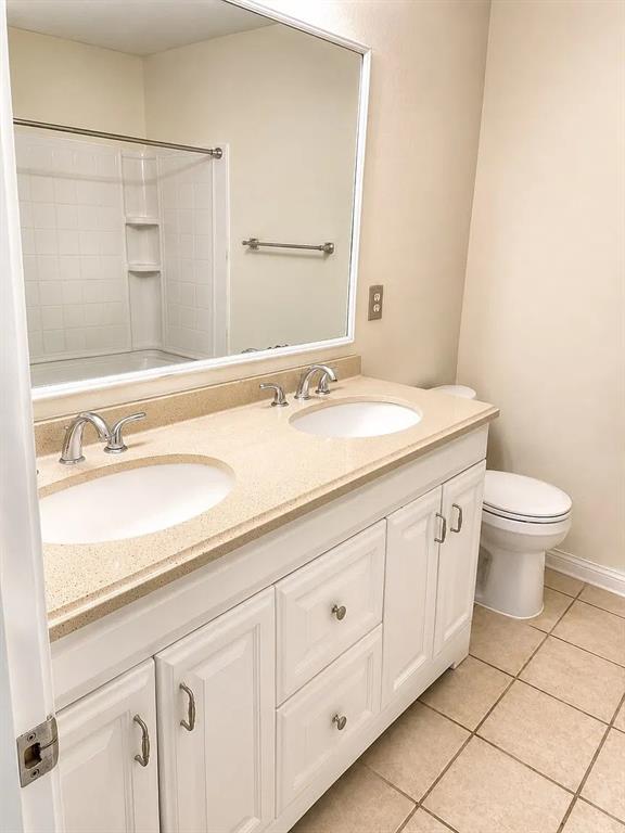 Double vanity featuring white cabinetry, dual undermount sinks, solid surface countertop, large framed mirror, and tile flooring