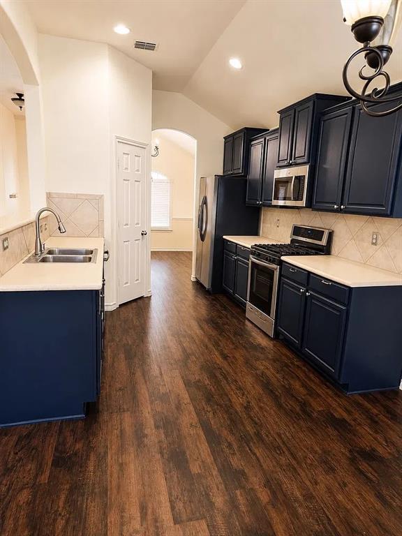 Kitchen featuring dark-toned cabinetry, light-colored countertops, stainless steel appliances, tile backsplash, and wood-finish flooring Kitchen featuring dark-toned cabinetry, light-colored countertops, stainless steel appliances, tile backsplash, and wood-finish flooring