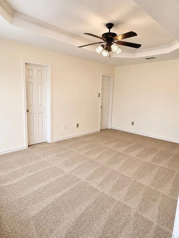 Tray ceiling with central light fixture and ceiling fan, wall-to-wall carpeting, and two interior six-panel doors