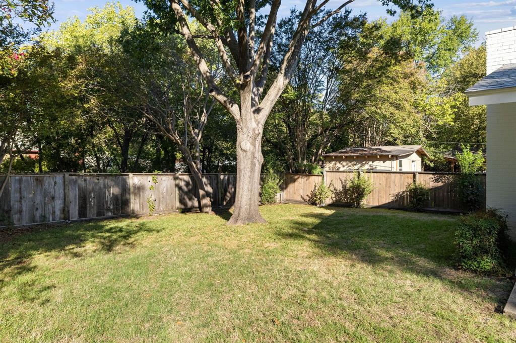 Backyard featuring a manicured lawn, wood fencing, mature trees, and an accessory structure