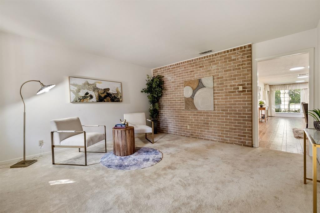 Living area featuring a floor-to-ceiling brick accent wall and neutral carpeting Living area featuring a floor-to-ceiling brick accent wall and neutral carpeting