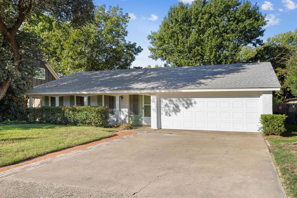 Single-story brick exterior featuring a covered front porch, arched entryway, attached two-car garage, and mature landscaping Single-story brick exterior featuring a covered front porch, arched entryway, attached two-car garage, and mature landscaping