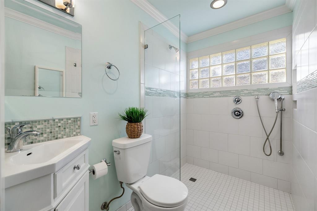 Bathroom featuring a vanity with integrated sink, glass-enclosed shower with tile surround, mosaic accent tiling, and glass block window