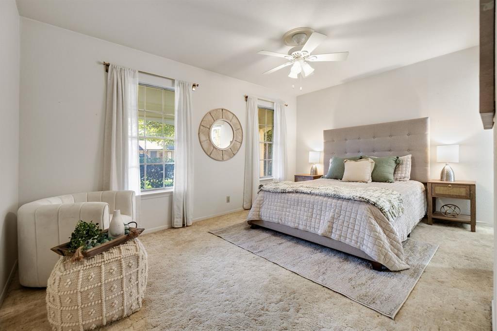 Neutral wall-to-wall carpeting, multiple windows providing natural light, and a central ceiling fan with integrated lighting