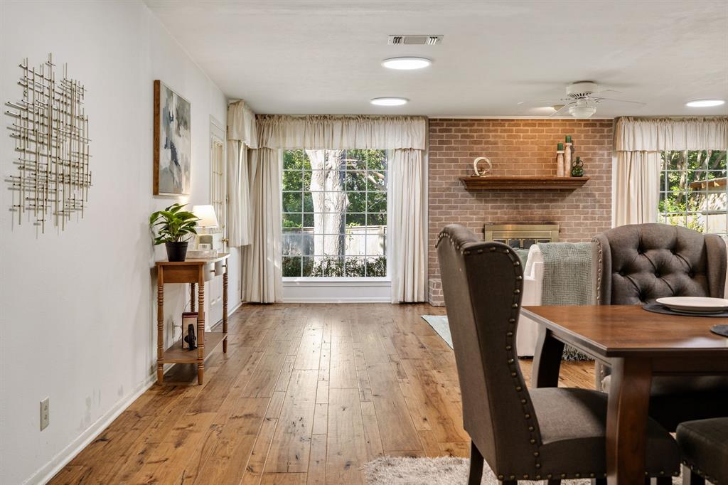 Living space featuring wood-finish flooring, a floor-to-ceiling brick accent wall, a built-in wood mantel, and large windows with natural light Living space featuring wood-finish flooring, a floor-to-ceiling brick accent wall, a built-in wood mantel, and large windows with natural light