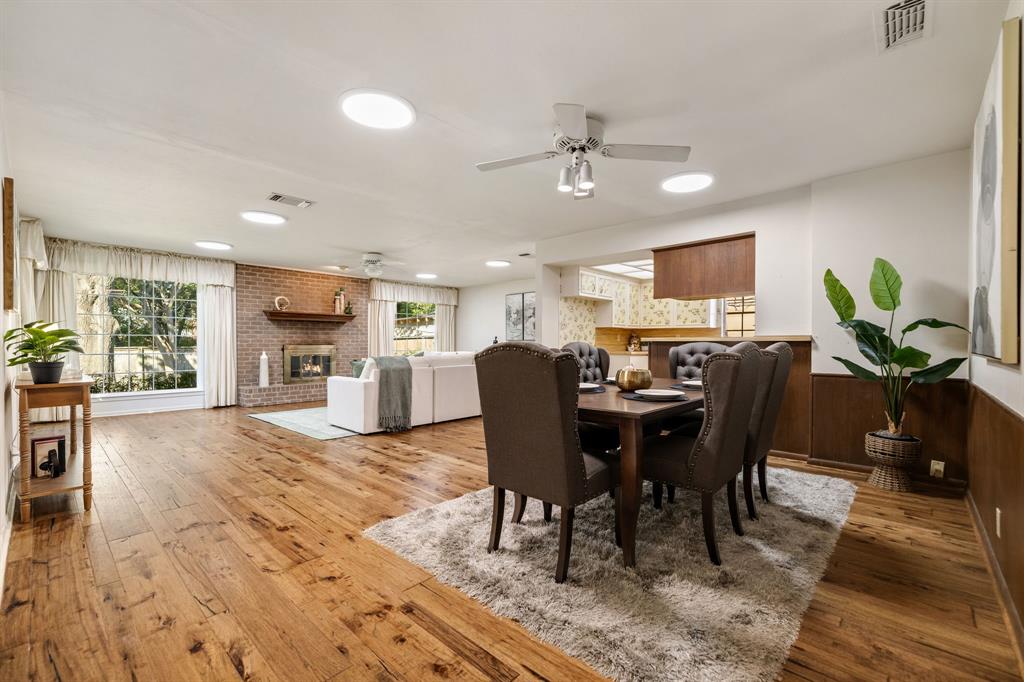 Spacious room featuring wood-finish flooring, a brick fireplace with a wood mantel, ceiling-mounted light fixtures, and lower-wall wood paneling Spacious room featuring wood-finish flooring, a brick fireplace with a wood mantel, ceiling-mounted light fixtures, and lower-wall wood paneling