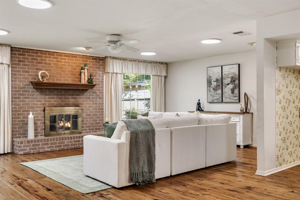 Living space featuring wood-finish flooring, a floor-to-ceiling brick fireplace with a wood mantel, a brass-finish fireplace enclosure, and recessed lighting Living space featuring wood-finish flooring, a floor-to-ceiling brick fireplace with a wood mantel, a brass-finish fireplace enclosure, and recessed lighting