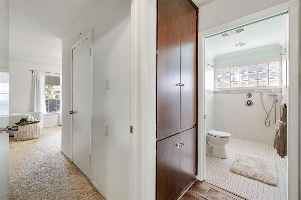 Built-in floor-to-ceiling wood cabinetry, bathroom featuring a glass block window, wall-mounted shower fixture with handheld sprayer, white tile flooring, and neutral wall tones