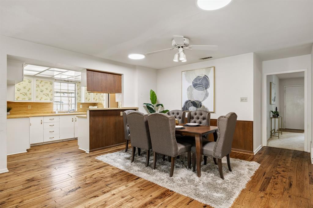 Dining area featuring wood-finish flooring, wainscoting, a ceiling fan with integrated lighting, and a kitchen pass-through with built-in cabinetry Dining area featuring wood-finish flooring, wainscoting, a ceiling fan with integrated lighting, and a kitchen pass-through with built-in cabinetry