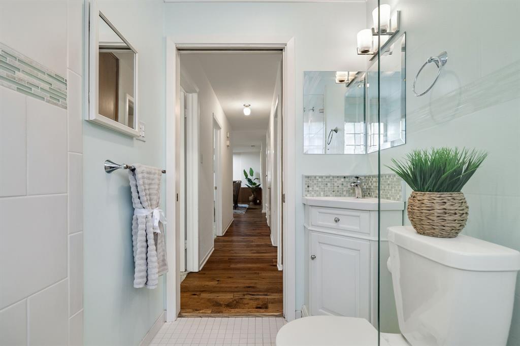 Bathroom featuring a white corner vanity with a mosaic tile backsplash, a glass-enclosed shower, wall-mounted lighting, and wood-finish flooring