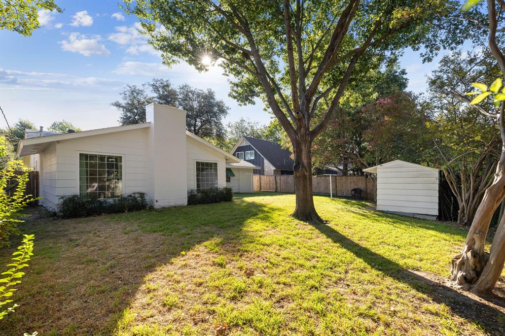 Backyard featuring white horizontal siding, a central masonry chimney, mature trees, a detached storage structure, and wood privacy fencing