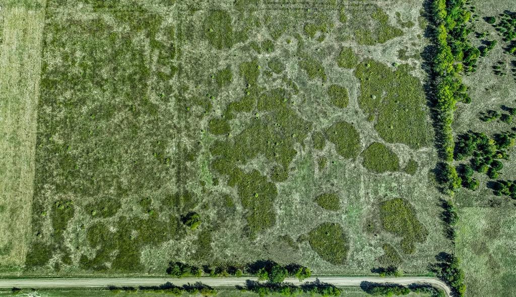 Aerial perspective of expansive acreage featuring meadow terrain, clusters of native vegetation, and mature tree lines bordering a gravel road frontage Aerial perspective of expansive acreage featuring meadow terrain, clusters of native vegetation, and mature tree lines bordering a gravel road frontage