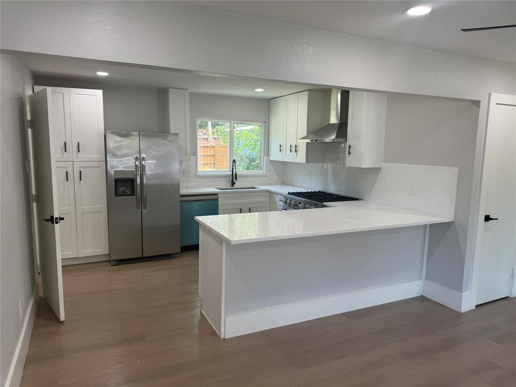 Kitchen featuring white shaker-style cabinetry, quartz countertops, stainless steel appliances, a subway tile backsplash, and wood-finish flooring