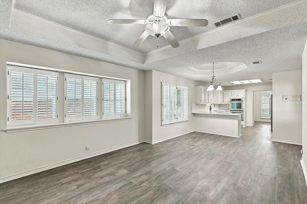 Tray ceilings with integrated lighting, wood-finish flooring, plantation shutters, and recessed kitchen cabinetry