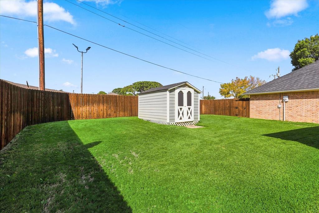 Spacious backyard featuring a manicured lawn, full-perimeter wood fencing, and a detached storage structure