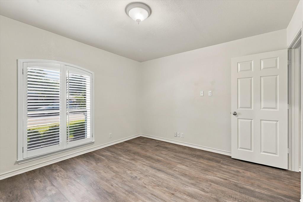 Room featuring wood-finish flooring, arched window with plantation shutters, six-panel interior door, and flush-mount ceiling light fixture