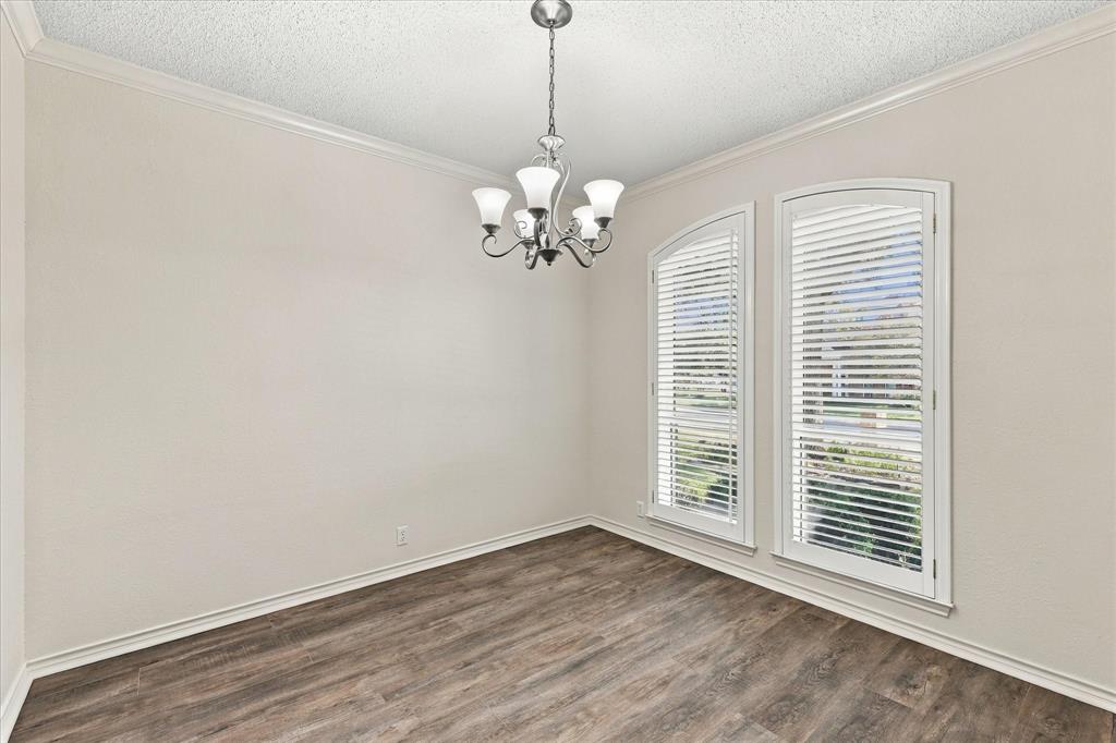 Room featuring wood-finish flooring, crown molding, a five-arm metal chandelier, and dual arched windows with white shutters