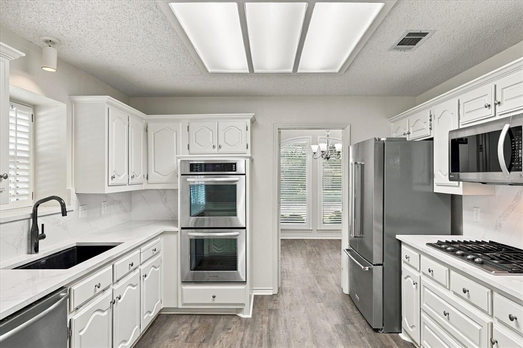 Kitchen featuring white cabinetry, quartz countertops, stainless steel double wall ovens, a stainless steel gas cooktop, and a matte black faucet with an undermount sink