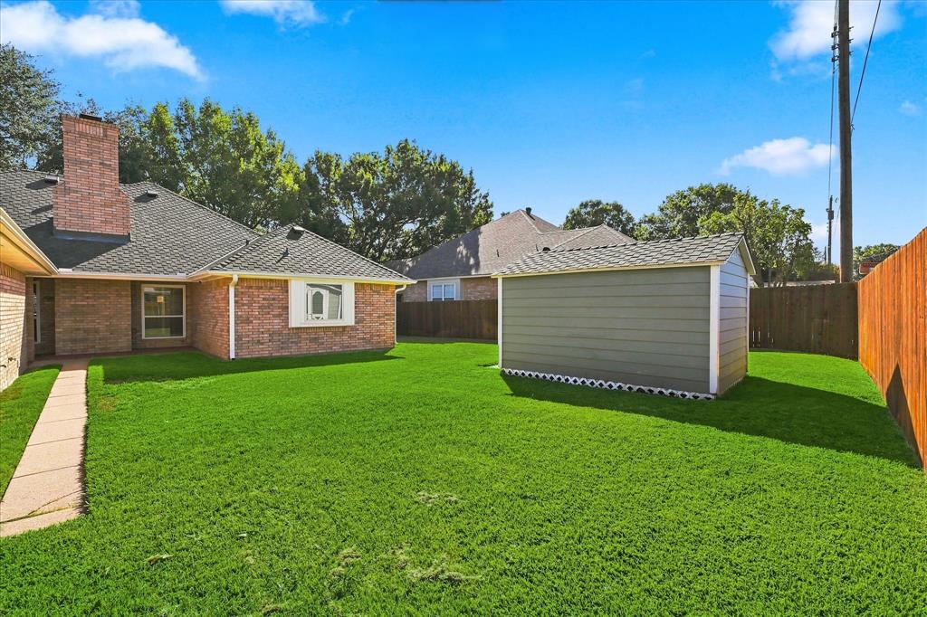 Backyard featuring a brick-exterior house, detached storage structure, concrete walkway, and wood perimeter fencing