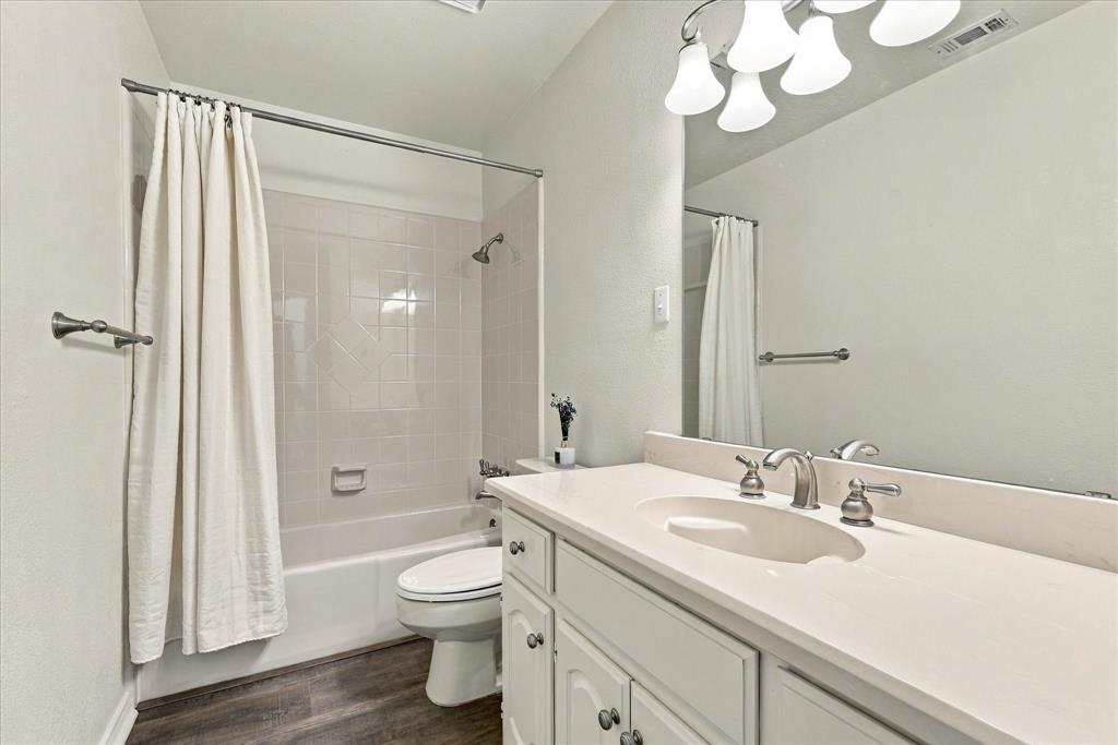 Bathroom featuring a single-basin vanity with a solid-surface countertop, full-width wall mirror, wood-finish flooring, and a tiled shower-tub combination