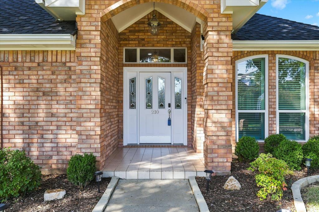 Brick exterior featuring a covered entryway with an arched portico, a white entry door with decorative glass inserts, an arched transom window, and a tiled porch surface