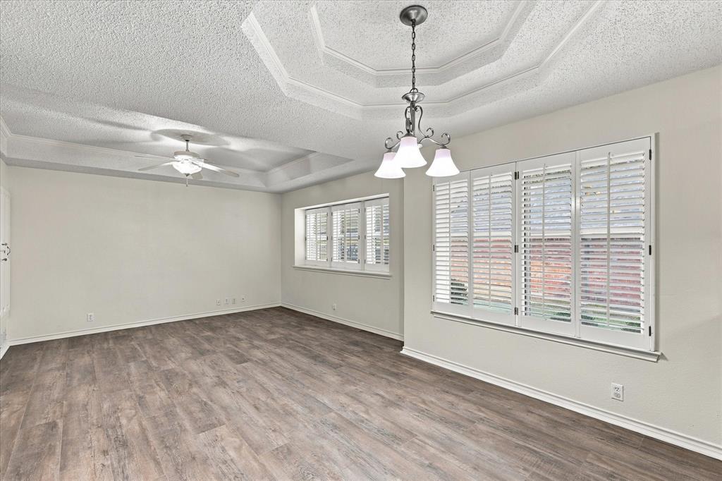 Tray ceiling featuring a central tiered design, wood-finish flooring, plantation shutters, and a multi-light chandelier