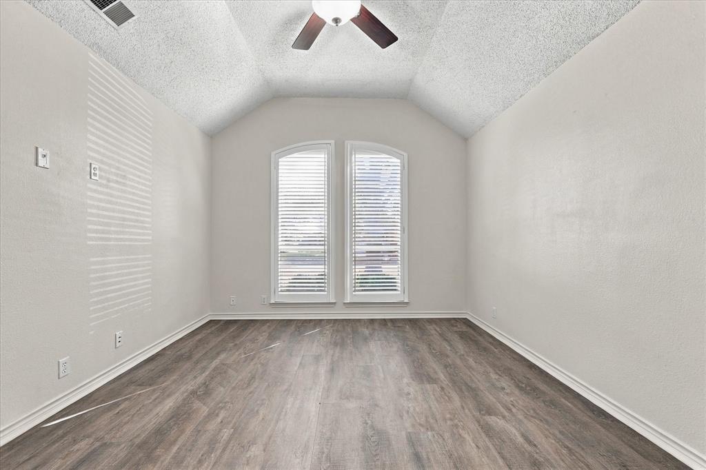 Vaulted ceilings, wood-finish flooring, two arched windows with horizontal blinds, and a central ceiling fan with integrated light fixture
