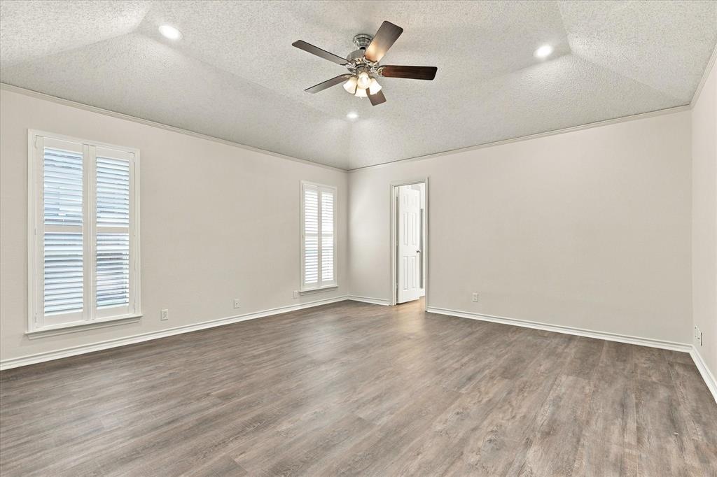 Vaulted ceiling featuring a central multi-blade ceiling fan, recessed lighting, wood-finish flooring, and windows with white plantation-style shutters