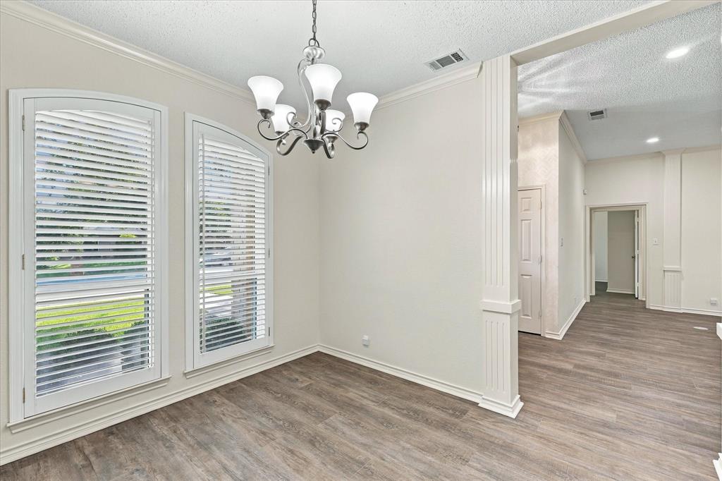 Arched windows with shutters, wood-finish flooring, and a multi-light chandelier featuring a fluted architectural column