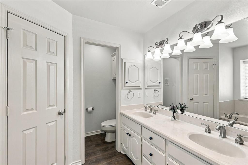 Dual-sink vanity with a solid-surface countertop, white raised-panel cabinetry, full-width mirror, and five-light vanity fixture