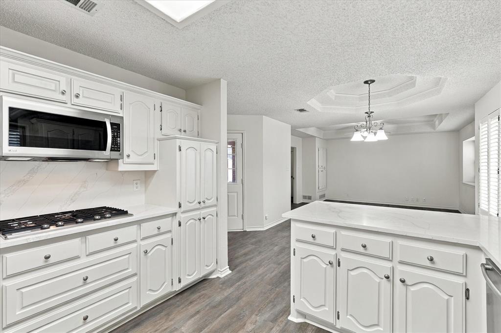 Kitchen featuring white cabinetry, solid-surface countertops, integrated stainless steel microwave, gas cooktop, and wood-finish flooring