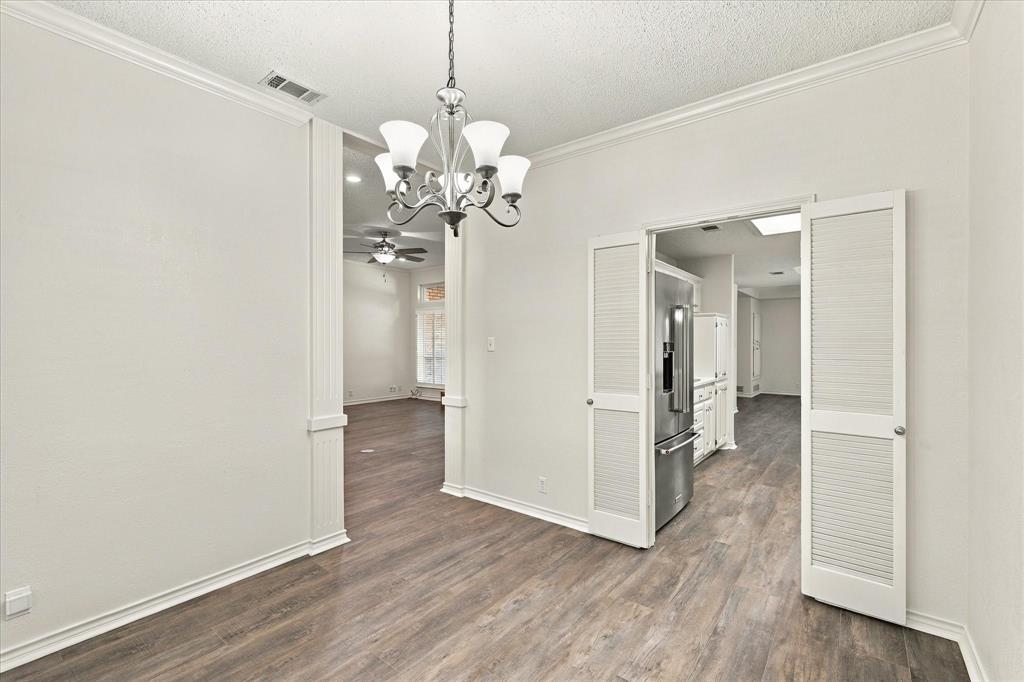 Interior space featuring wood-finish flooring, crown molding, and a tiered chandelier with glass shades, complemented by white louvered double doors