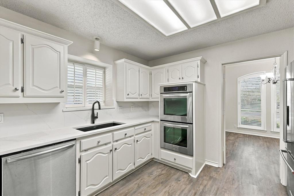 Kitchen featuring white cabinetry with raised-panel detailing, light-toned stone-finish countertops, stainless steel double wall ovens, a matte black faucet with an undermount sink, and recessed panel lighting