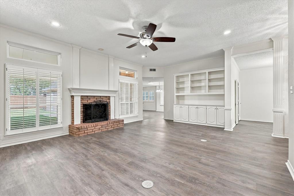 Brick fireplace with decorative mantel, wood-finish flooring, built-in cabinetry, dual window sets with plantation shutters, and recessed lighting