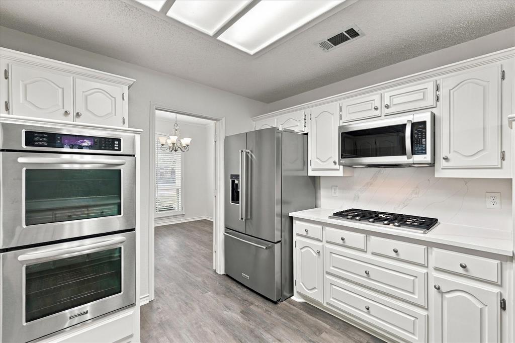 Kitchen featuring white cabinetry, stainless steel double wall ovens, a stainless steel refrigerator, a built-in microwave, and stone-finish countertops