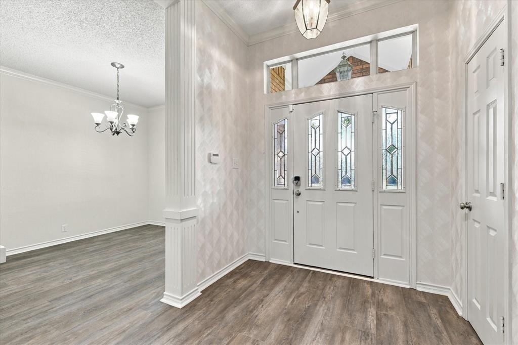 Entryway featuring a front door with decorative glass panels, a transom window, wood-finish flooring, a fluted column, and a multi-arm chandelier