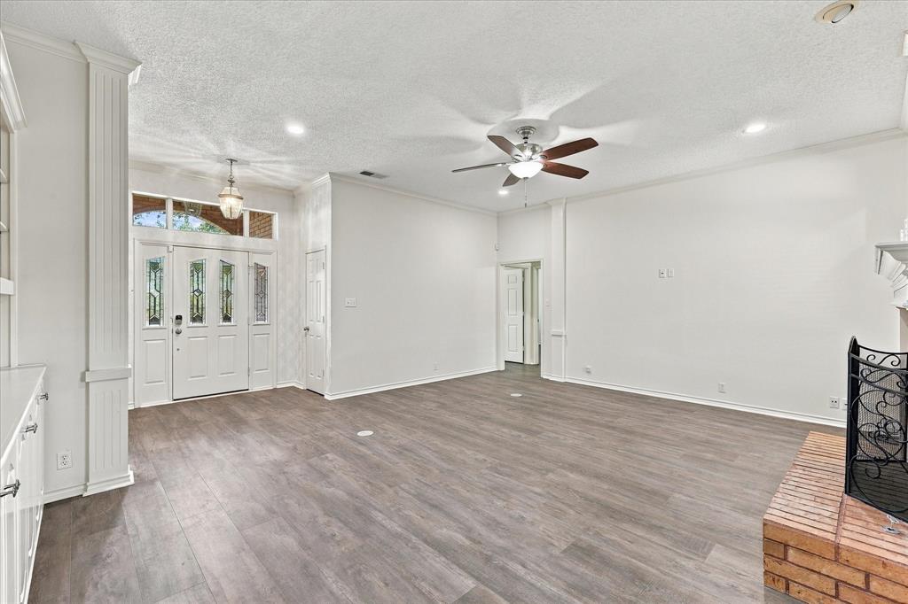 Living area featuring wood-finish flooring, a brick fireplace, a multi-pane front door with glass inserts, architectural columns, and a ceiling fan with integrated lighting