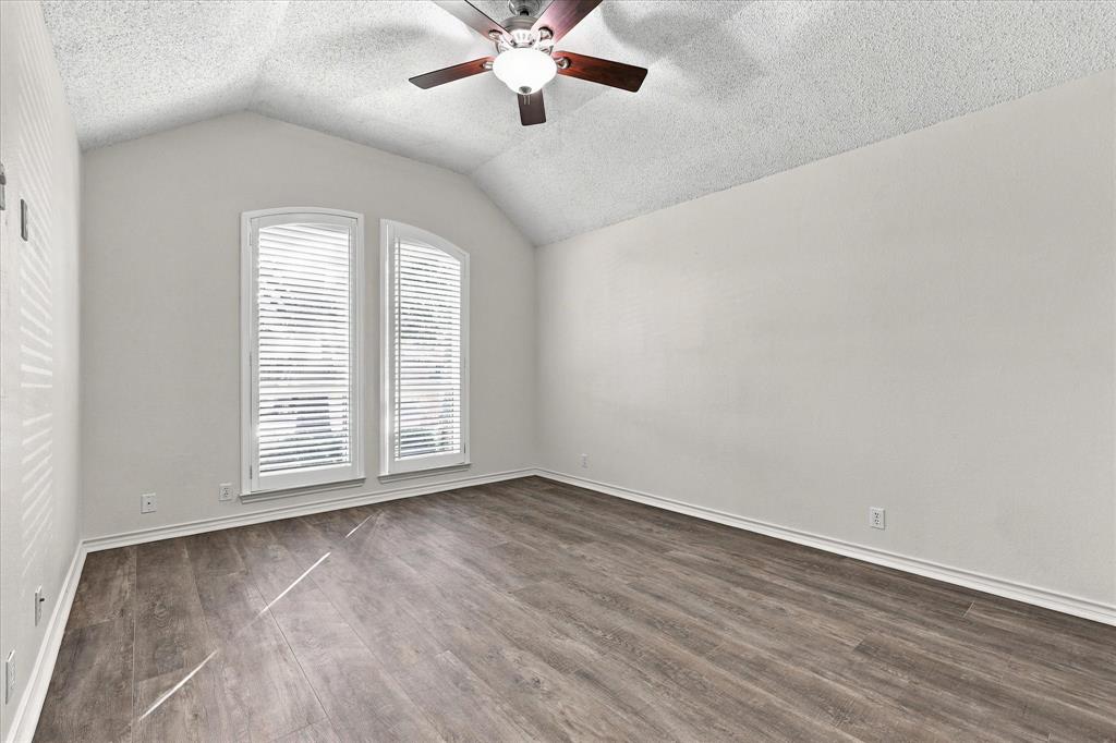 Vaulted ceiling featuring a central ceiling fan with integrated lighting, wood-finish flooring, and arched-top windows
