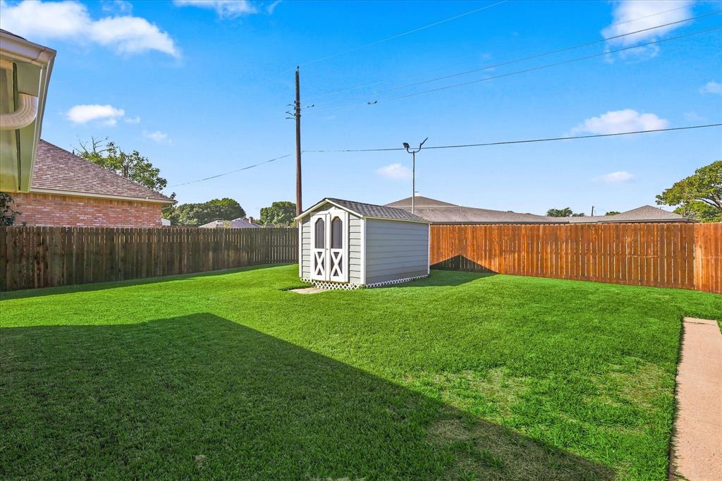 Fenced backyard featuring a manicured lawn, a detached storage shed, and a concrete pathway