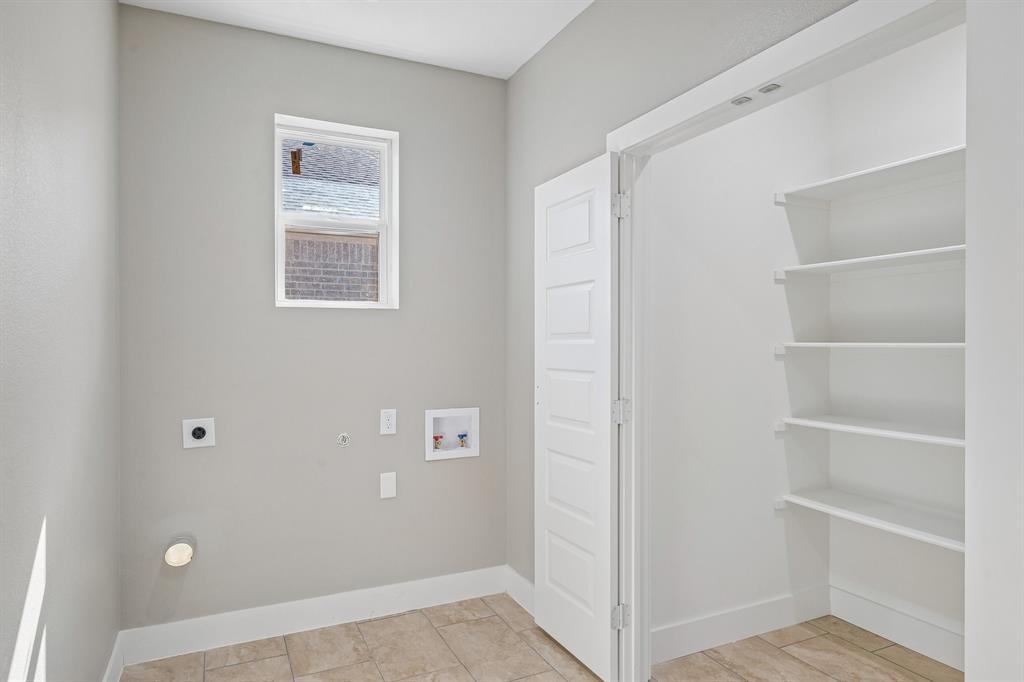 Utility room featuring neutral wall paint, tile flooring, a window, and built-in white shelving