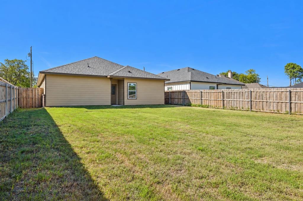 Expansive backyard featuring a level lawn, full wood-plank privacy fencing, and a neutral-toned exterior with a shingled hip roof