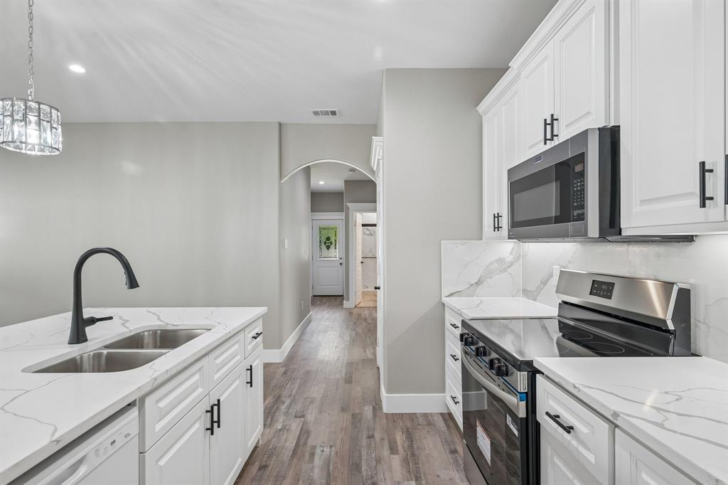 Kitchen featuring white shaker-style cabinetry, white countertops with grey veining, a stainless steel microwave and range, and wood-finish flooring