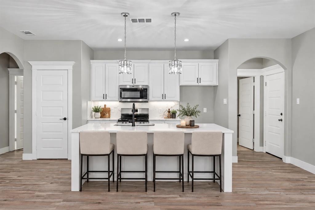 Kitchen featuring white cabinetry, an oversized quartz-topped island, wood-finish flooring, stainless steel appliances, and dual pendant lighting