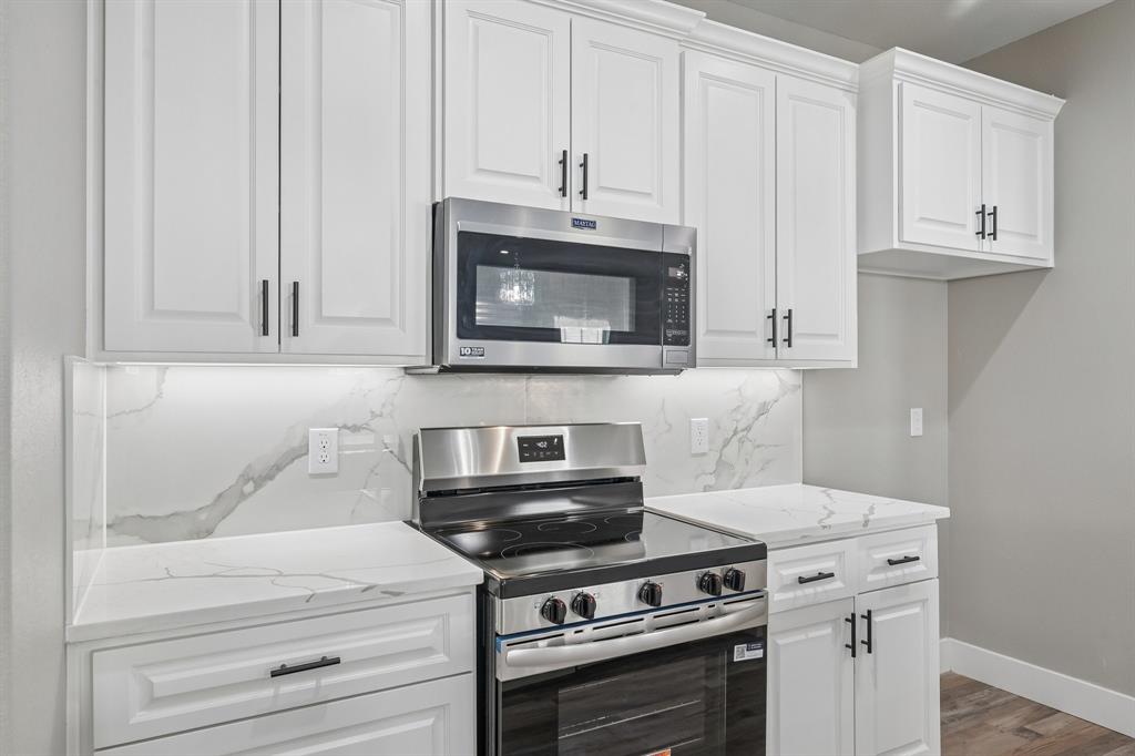 Kitchen featuring white shaker-style cabinetry, matte black hardware, integrated stainless steel appliances, stone-patterned backsplash, and matching stone-patterned countertops