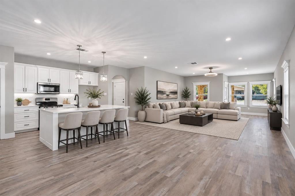 Open concept living area featuring wood-finish flooring, white cabinetry, center island with stone countertop, stainless steel appliances, and recessed lighting