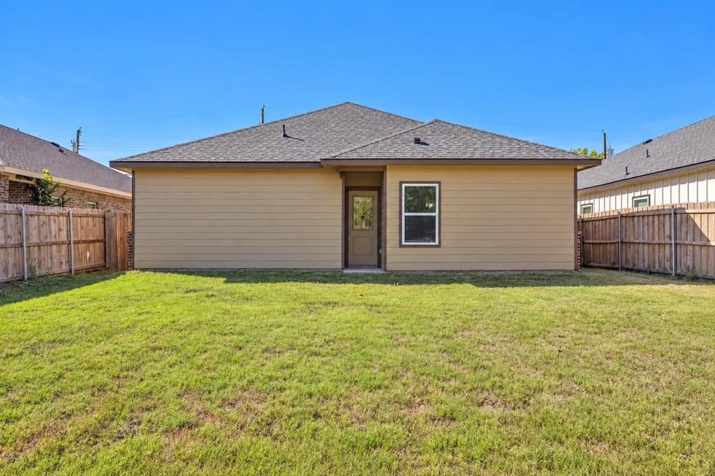 Exterior rear elevation featuring horizontal siding, a hipped roof, a single-entry door with glass insert, and a fenced backyard with grass lawn