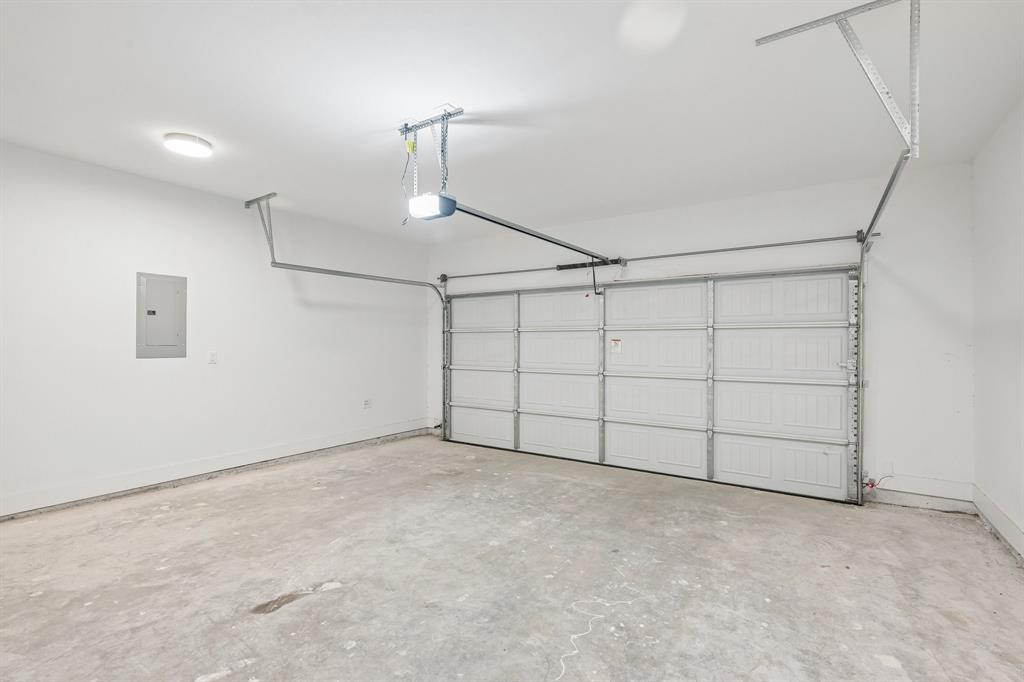 Two-car garage featuring a sectional door, automatic opener, concrete flooring, and an integrated electrical service panel